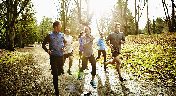 Smiling group of male and female runners trail running together in park