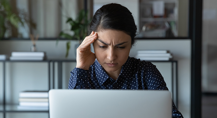 Close up stressed puzzled Indian businesswoman looking at laptop screen, sitting in office, exhausted upset employee reading bad news in email, having problem with difficult online project
