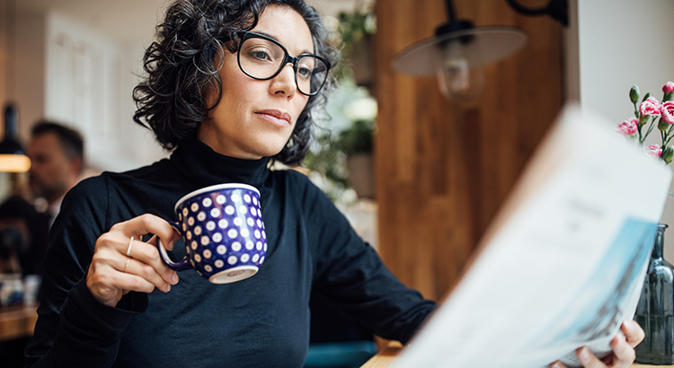 Mid adult businesswoman sitting at cafe reading newspaper and having coffee. Female business professional reading a newspaper in coffee shop.