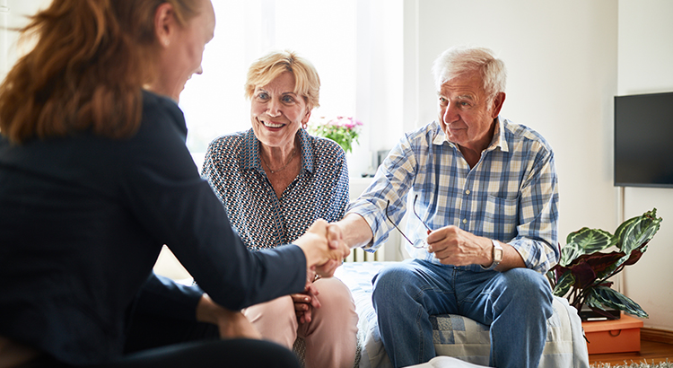 Financial advisor shaking hands with senior man in living room. Retired couple in meeting with a female financial advisor at home.