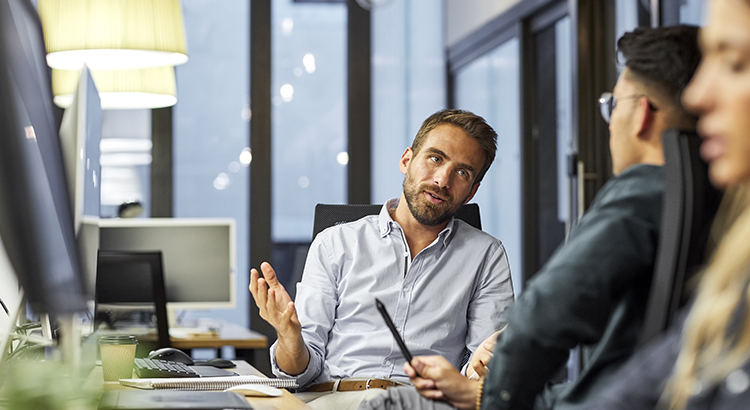Businessman explaining colleague while sitting at desk. Male business professionals are discussing during meeting. They are sitting in office.