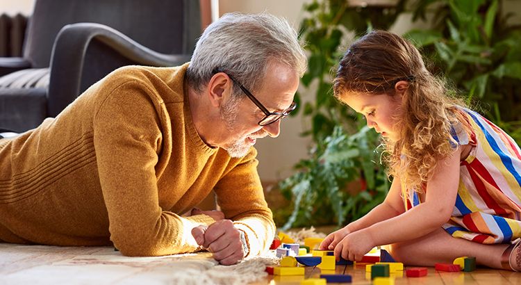 Mature man lying on floor playing with little girl, support, assistance, learning