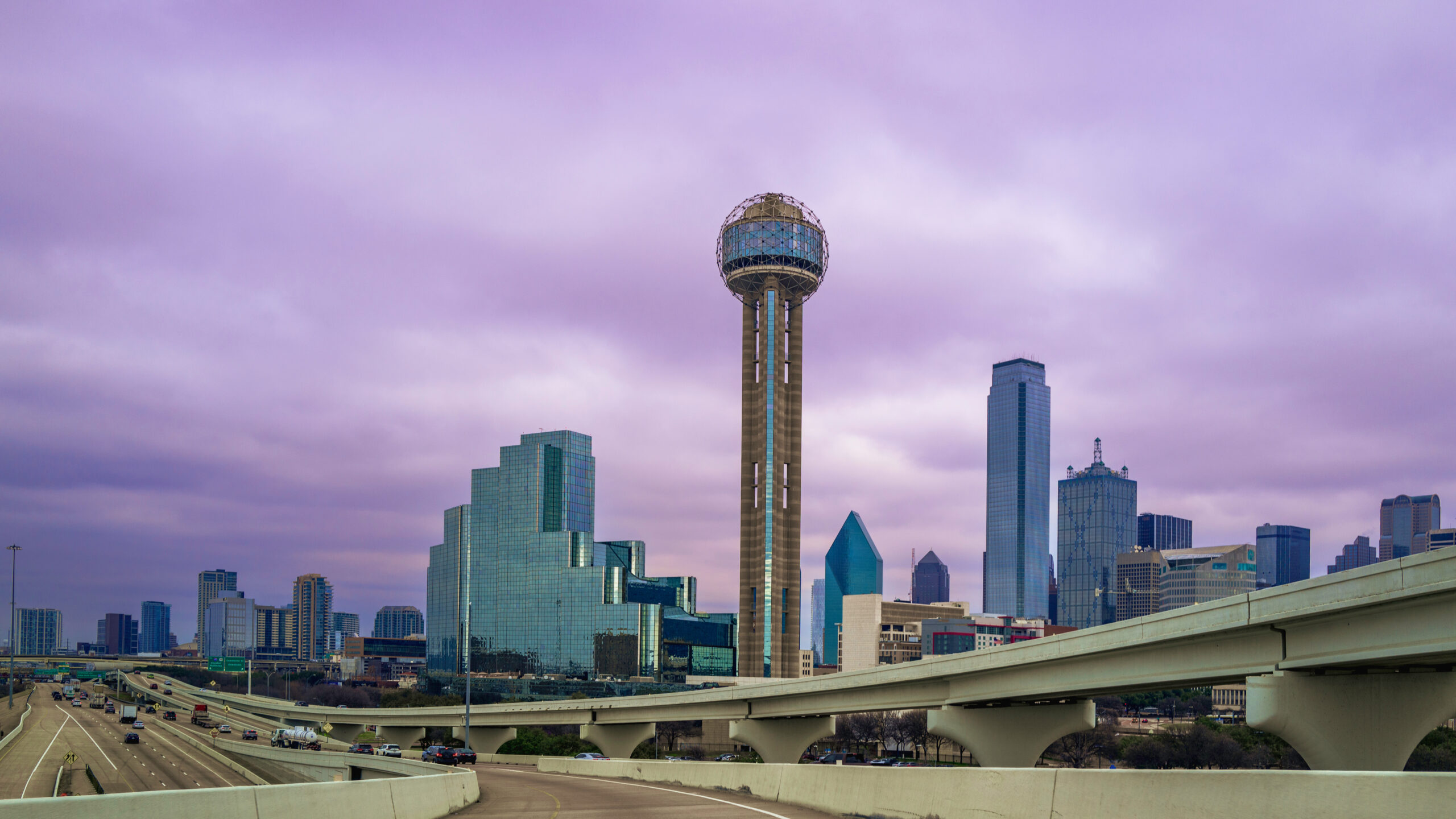 Moody cityscape of Dallas downtown skyline over the highways with purple clouds at dusk, a view from the Margaret Hunt Hill Bridge in Texas, USA, roadtrip landscape photography