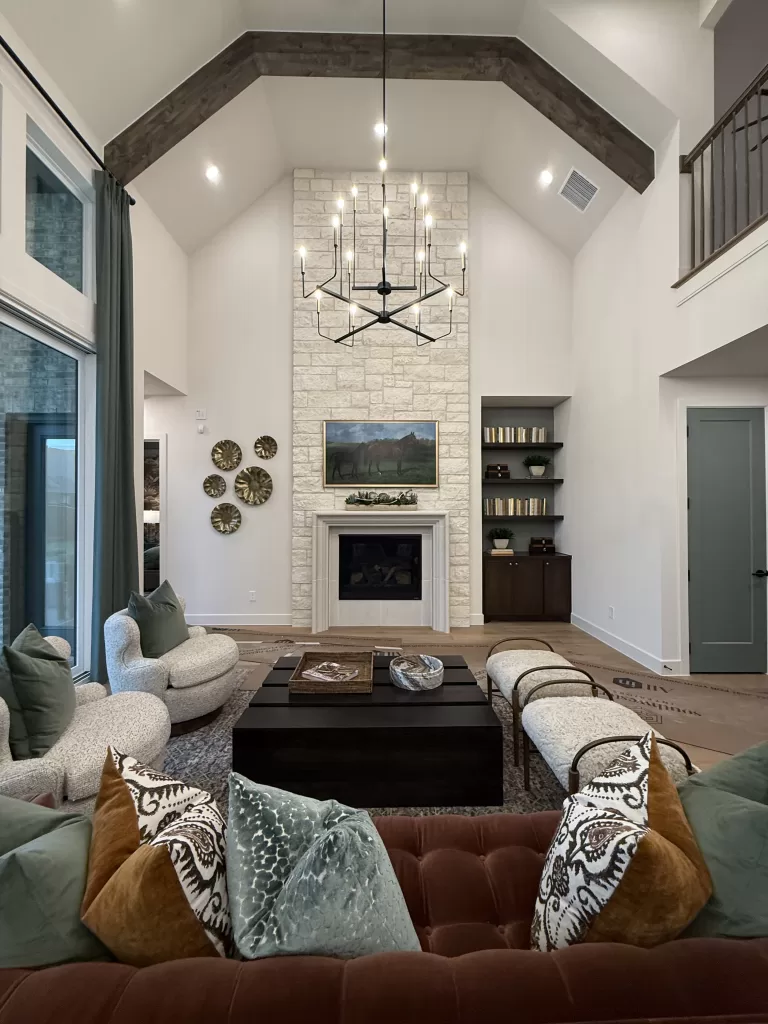 Highland Homes model living room in Furst Ranch Flower Mound with stone fireplace, vaulted ceiling, chandelier, and designer seating.