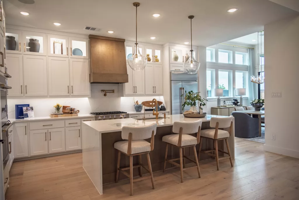 Kitchen and dining area in a David Weekley Homes model at Furst Ranch, featuring a large island, wood vent hood, pendant lighting, and open-concept layout near Flower Mound and Bartonville, TX.