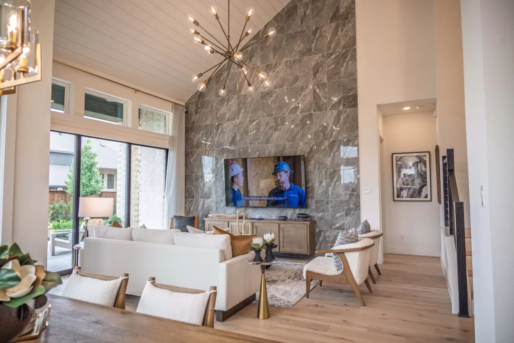Living room in a David Weekley Homes model at Furst Ranch, featuring soaring ceilings, a dramatic tile fireplace wall, modern chandelier, and open-concept design near Flower Mound and Bartonville, TX.