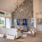Living room in a David Weekley Homes model at Furst Ranch, featuring soaring ceilings, a dramatic tile fireplace wall, modern chandelier, and open-concept design near Flower Mound and Bartonville, TX.