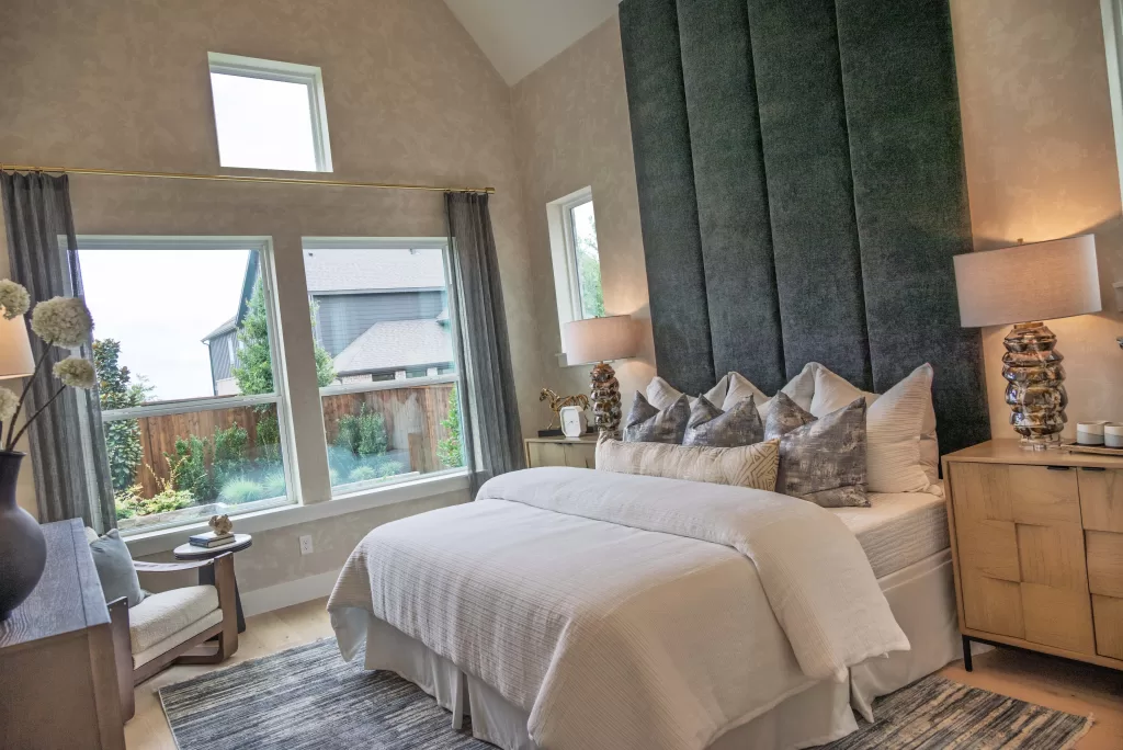 Primary suite in a David Weekley Homes model at Furst Ranch, featuring vaulted ceilings, large windows, upholstered accent wall, and designer finishes near Flower Mound and Bartonville, TX.