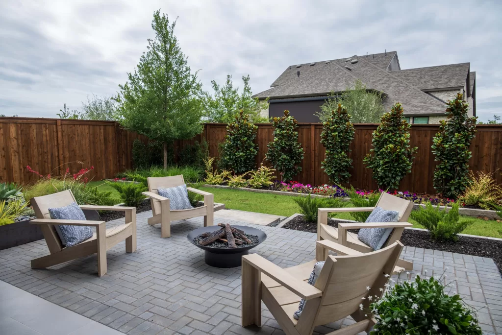 Outdoor living space at a David Weekley Homes model in Furst Ranch, featuring a landscaped backyard, paver patio, fire pit seating area, and private fenced yard near Flower Mound and Bartonville, TX.